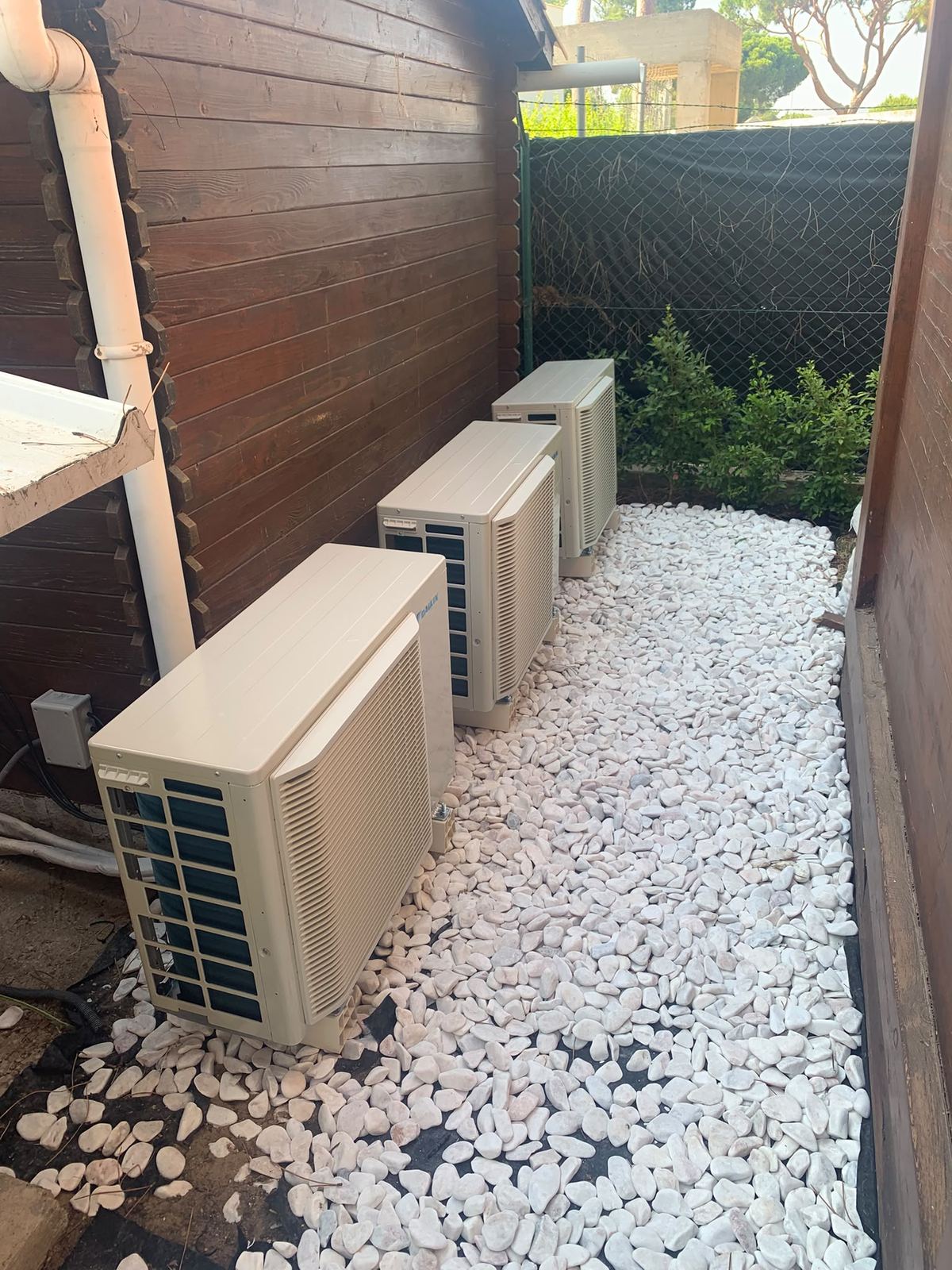 Three Daikin outdoor units on a stone bed